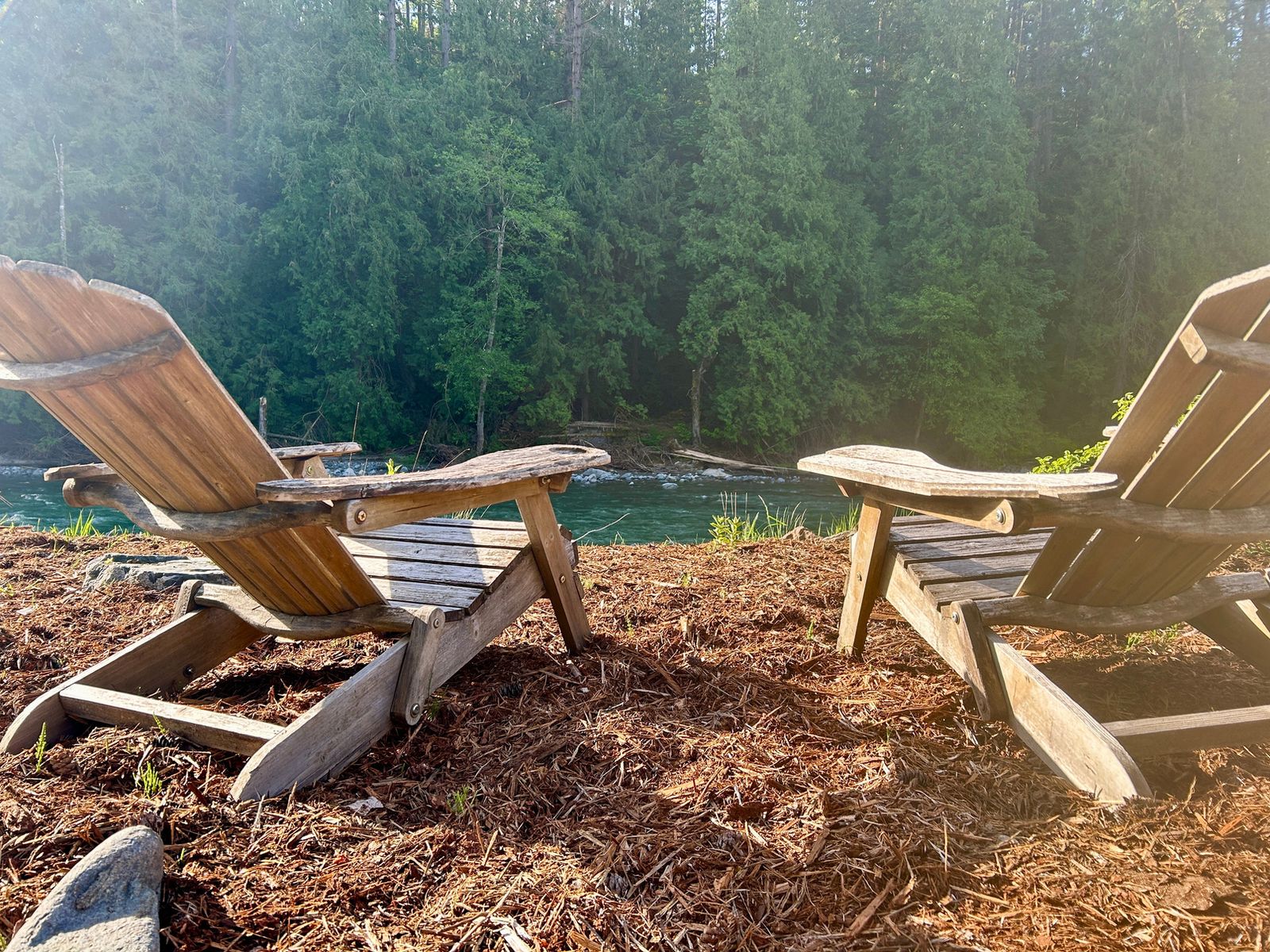 Two wooden chairs facing the river at golden hour